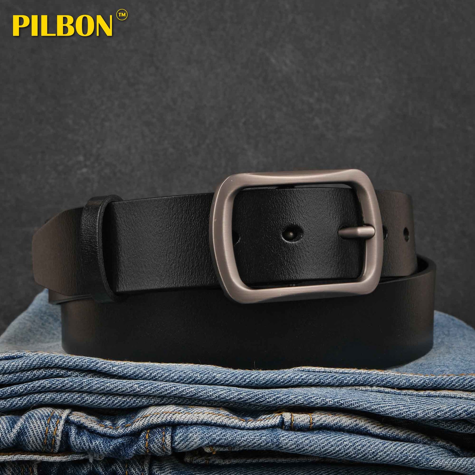 Black leather PILBON G311 belt with stainless alloy buckle, laying on folded denim, stylish and durable accessory.