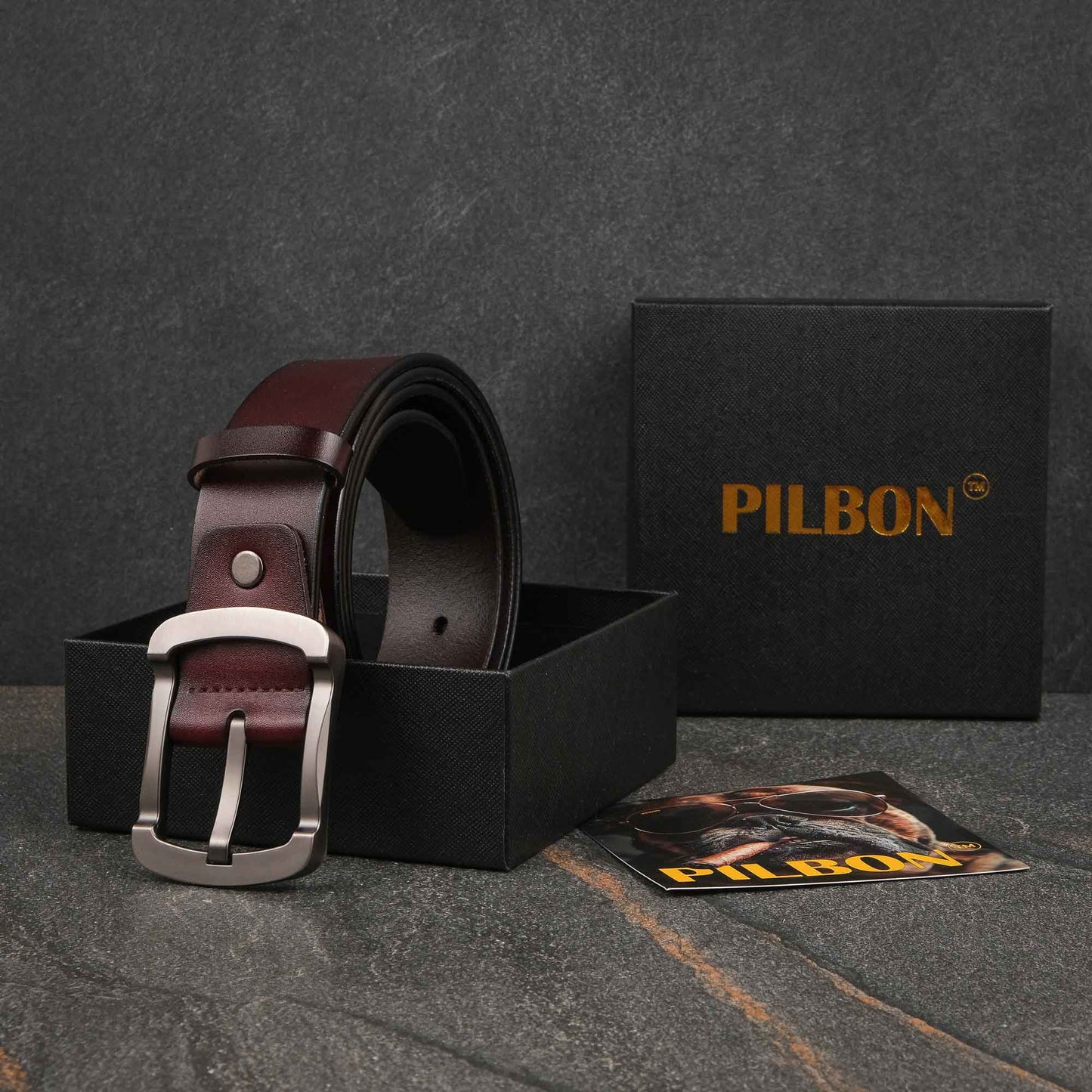 Brown leather belt G319 in a black PILBON box with stainless steel buckle and product pamphlet on a textured surface.